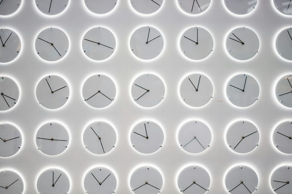 A wall of clocks showing different times in a minimalist, light-colored style